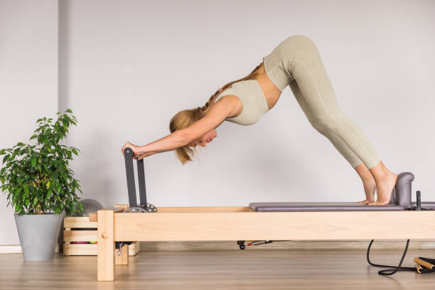 Woman training pilates on the reformer bed. Reformer pilates studio machine for fitness workouts in gym. Fit, healthy and strong authentical body. Fitness concept stock photo