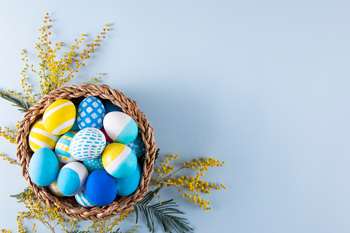 Easter eggs in a basket on blue background with flowers