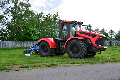A red tractor with black wheels is parked on a grass on the field isolated, close-up