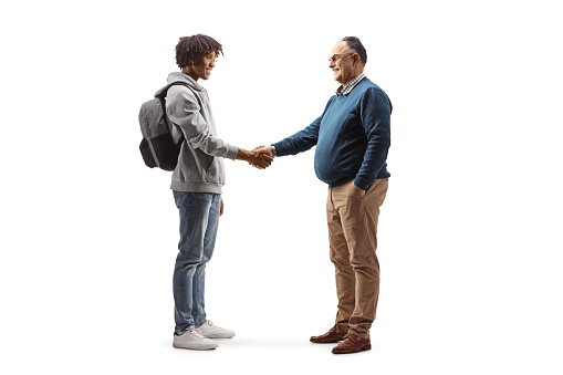 Full length profile shot of an african american male student and a mature man shaking hands isolated on white background