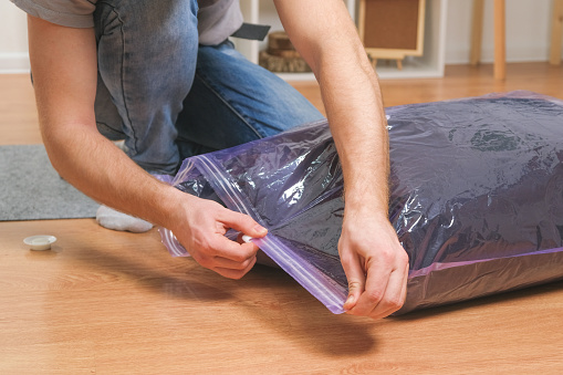 A man folds winter jackets and puts them in a vacuum bag for seasonal storage in the closet.