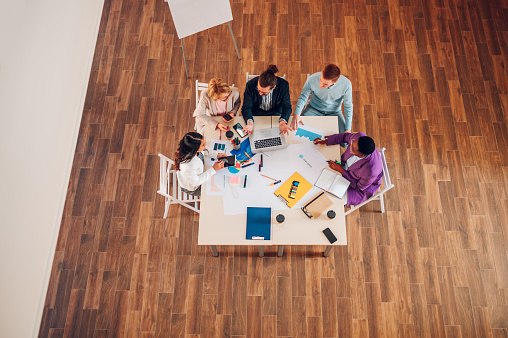 High angle shot of a multiracial professional project managers group negotiating in boardroom at meeting. Boss discussing with creative diverse team the concept of business strategy in their project