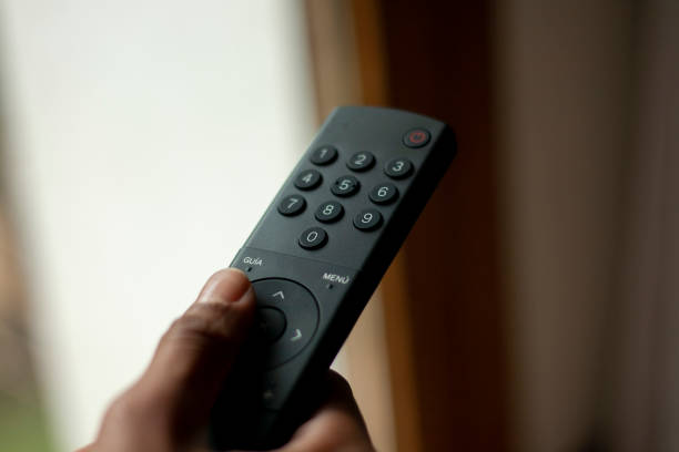 istock hand directing a television remote where you can see the different keyboard controls, with a blurred background 1473887830