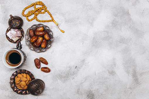 Table top view image of decoration Ramadan Kareem, dates fruit, cup of coffee and almond on gray stone background. Flat lay with copy space.