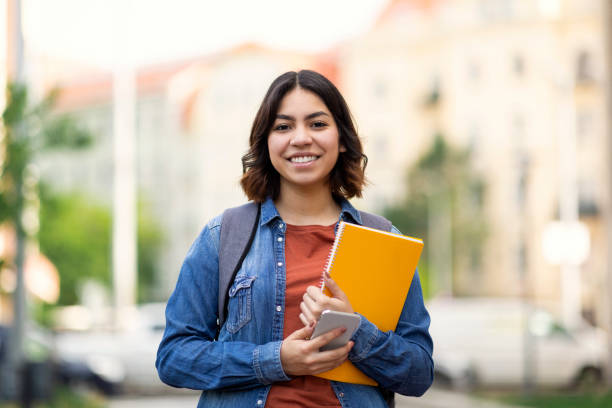 istock Beautiful Young Arab Female Student Standing Outdoors With Workbooks In Hands 1473893094