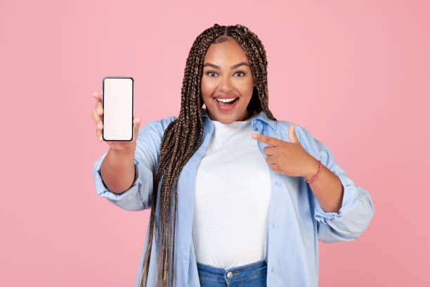 istock Joyful Black Lady Showing Mobie Phone Blank Screen, Pink Background 1473893181
