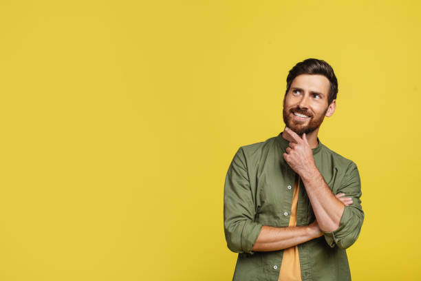 istock Pensive middle aged man thinking and touching chin, looking aside at free space, posing on yellow studio background 1473893211
