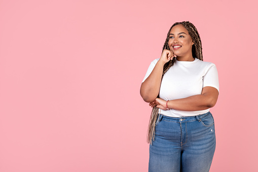 African American Plus Size Lady Dreaming And Thinking About Great Offer Looking Aside Holding Hand Near Face At Blank Space For Text Posing Standing Over Pink Background In Studio. Body Positive