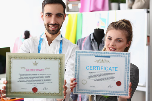 Man stylist and woman seamstress hold certificate of quality for clothes. Atelier tailoring high-quality fashionable designer clothes
