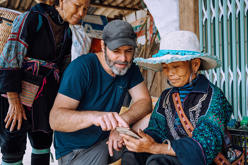 white european male tourist showing pictures on mobile phone to indigenous woman from the black hmong tribe in Sapa, northern Vietnam