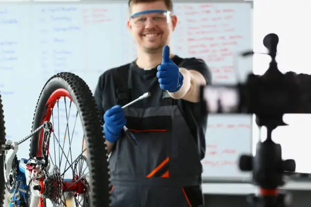 Photo of Male blogger holds thumbs up and repairs bicycle remotely