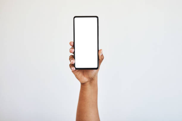 mão segurando telefone, tela em branco com maquete e mãos de mulher negra no estúdio isoladas no fundo branco. tecnologia, conecte-se e amplie o espaço no smartphone para site, mídia social ou publicidade - mão humana - fotografias e filmes do acervo