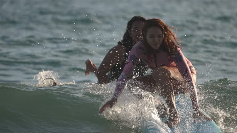 Asian Chinese female surfer riding wave in front of wave surfing instructor