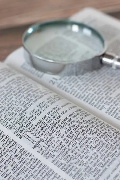 A closeup of the ten commandments verses in an open holy bible book with a magnifying glass. Vertical shot. Selective focus.