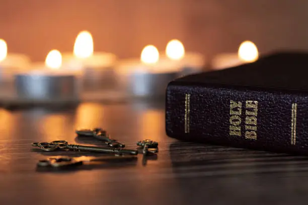 Holy bible book and ancient keys with burning candles on a dark background. A close-up.