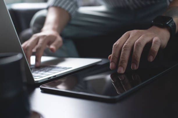istock Business man working on laptop computer and digital tablet pc on table at office with dark background, online working, close up 1473905110
