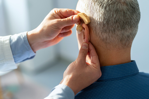 Male Doctor inserting hearing aid in man's ear