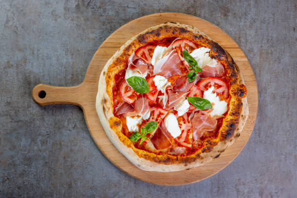 istock Delicious round pizza with prosciutto, mozzarella and basil on wooden board 1473906545