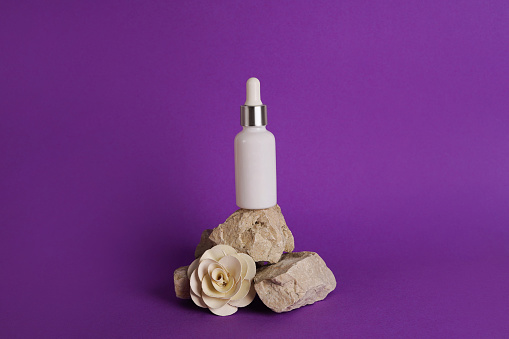 Glass dropper bottle with cosmetic oil, essential or serum staying on stone stand with dry flower on violet background. Herbal homeopathic products Natural organic spa cosmetics
