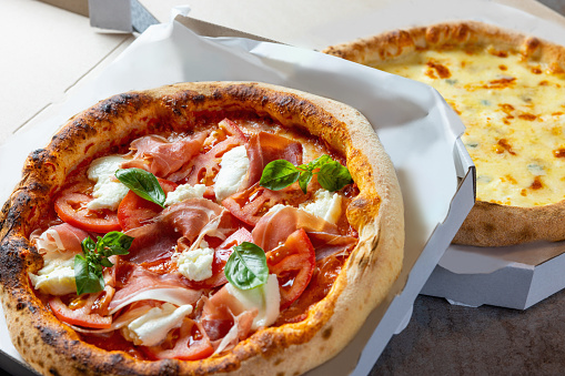 Fresh pizza in open delivery boxes, one with prosciutto and mozzarella the other one Margherita with cheese