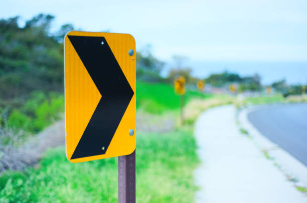 A row of chevrons form directional arrows to warn drivers about a dangerous curve in the road A row of chevrons form directional arrows to warn drivers about a dangerous curve in the road. Green hills and blue sky are visible in the background. road chevron warning signs stock pictures, royalty-free photos & images