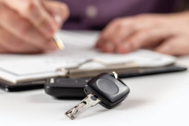 istock Car keys on desk with man signing purchase documents in background. 1473908451