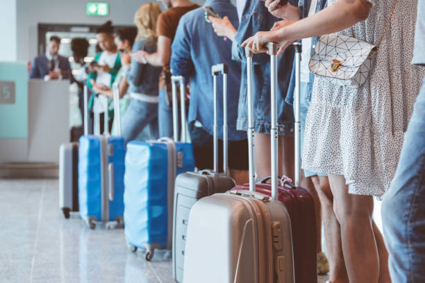 Passengers with luggage waiting in line at airport Travelers with luggage using smart phones while waiting in line for boarding at airport. Focus on wheeled luggage. airport stock pictures, royalty-free photos & images