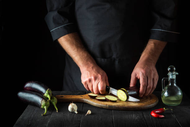 kucharz tnie bakłażana w kuchni restauracji. zbliżenie rąk szefa kuchni podczas pracy. pyszne śniadanie lub kolacja. - eggplant group of objects raw food eating zdjęcia i obrazy z banku zdjęć