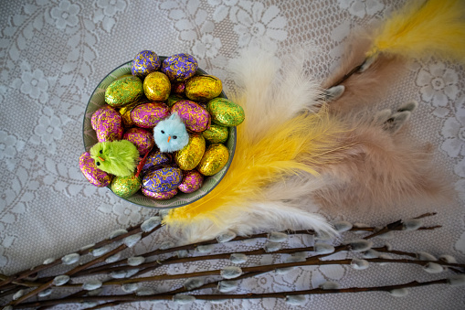 Easter chocolate eggs in colorful wrappings and willow branch with colorful feathers