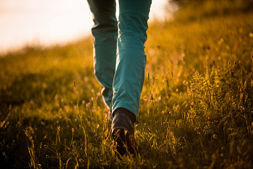 Part of young woman wearing sports clothes and shoes hiking the hill at sunset. Close up of hiking boots, unrecognizable person.