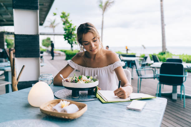 istock Happy ethnic woman writing thoughts in notebook during lunch in summer cafe 1473921349