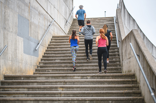 Mixed age range group of people moving up and exercising on concrete stairs. They are doing physical exercise to improve their health condition, wellbeing and energy levels.