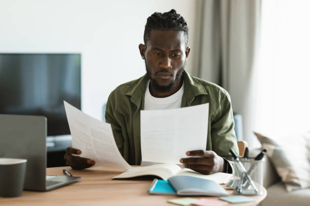 istock Focused black male entrepreneur reading papers and business reports, checking documents while sitting at desk at home 1473924200