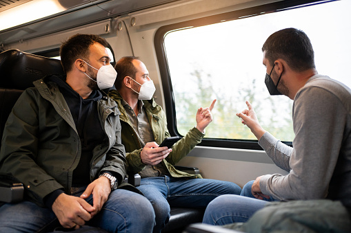 Group of mid-adult Caucasian men traveling together with train, while wear N95 protective face mask