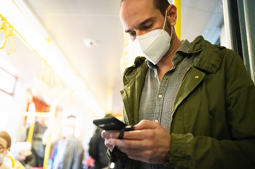 Mid-adult Caucasian man using mobile phone, in the bus, while wear N95 protective face mask