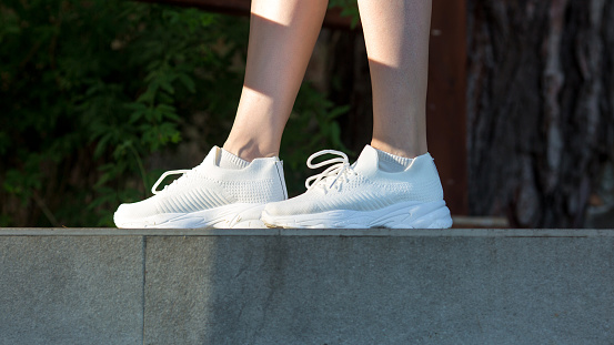 Women feet shod in white soft sneakers on sidewalk.