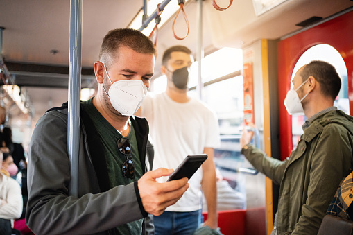 Mid-adult Caucasian man using mobile phone, in the train, while wear N95 protective face mask