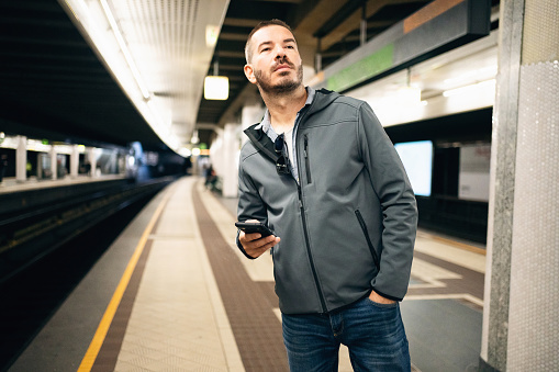 Portrait of mid-adult Caucasian man using mobile phone, at the subway station