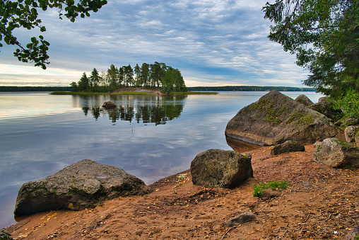 Stones on the shore and island with pine forest in beautiful fresh blue lake, Park Mon Repos, Vyborg, Russia.