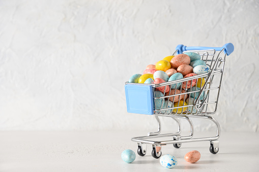 Easter composition with colorful pastel chocolate eggs in shopping trolley on white background. Copy space. Close up. Happy Easter. Greeting card.