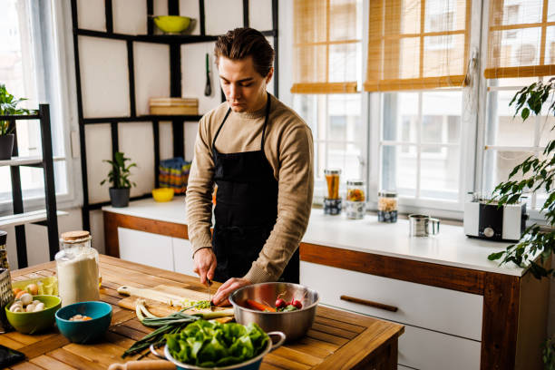 istock Handsome young man cutting vegetables for healthy meal in kitchen 1473928587