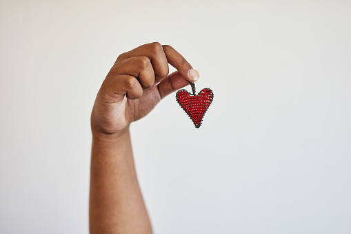 Hand, heart and keyring with a black woman in studio on a gray background holding a symbol of love. Emoji, shape and accessory with an african american person showing a red souvenir against a wall