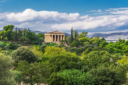 Athens Greece Temple Of Hephaestus day view surrounded by greenery on a bright sunshine over puffy clouds.