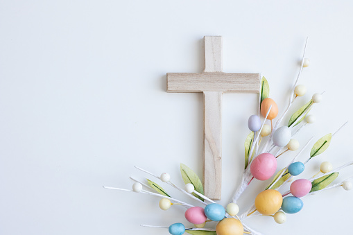 Wood Christian cross on a white background with sprigs of colourful easter eggs with copy space