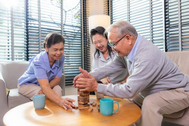 Elderly friends building tower from wooden cubes leisure time in nursing home. stock photo