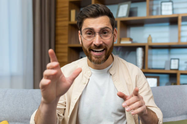 istock Mature teacher teaching online remotely, man with glasses and beard looking at web camera and smiling talking to colleagues and teaching, businessman at home sitting on sofa in living room 1473940021