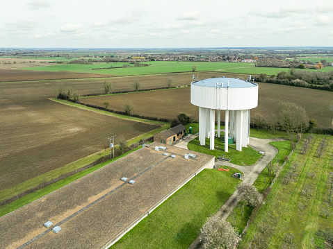 Drone view of a large concrete water tower seen together with a treatment plant in the English countryside.