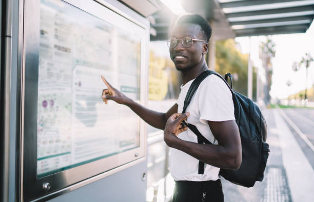 istock Handsome dark skinned male traveler with backpack checking location and destination on map, positive african american hipster guy checking public transport route on info banner on bus stop in city 1473941029