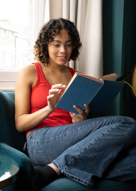istock Young woman relaxing at home reading a book 1473941175