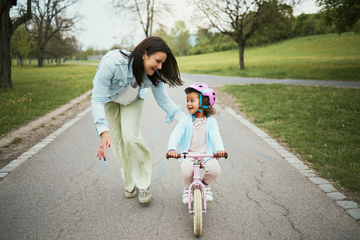 Children, bike and a mother teaching her girl how to cycle in a park while bonding together as a family. Nature, love and kids with a daughter learning how to ride a bicycle with her mom outside